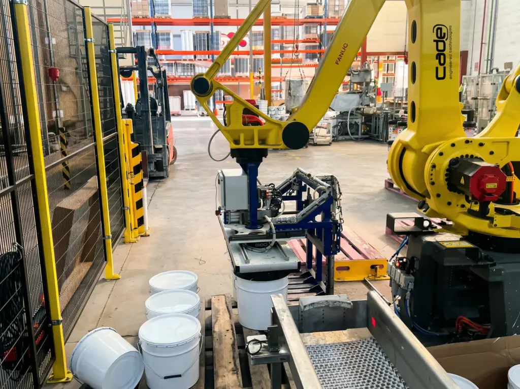 Robot industrial de paletizado manipulando botes de pintura en una celda automatizada